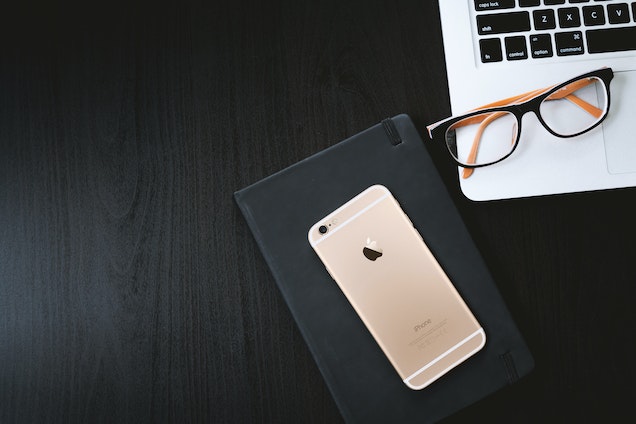 rose gold phone on a notebook with a laptop on a desk